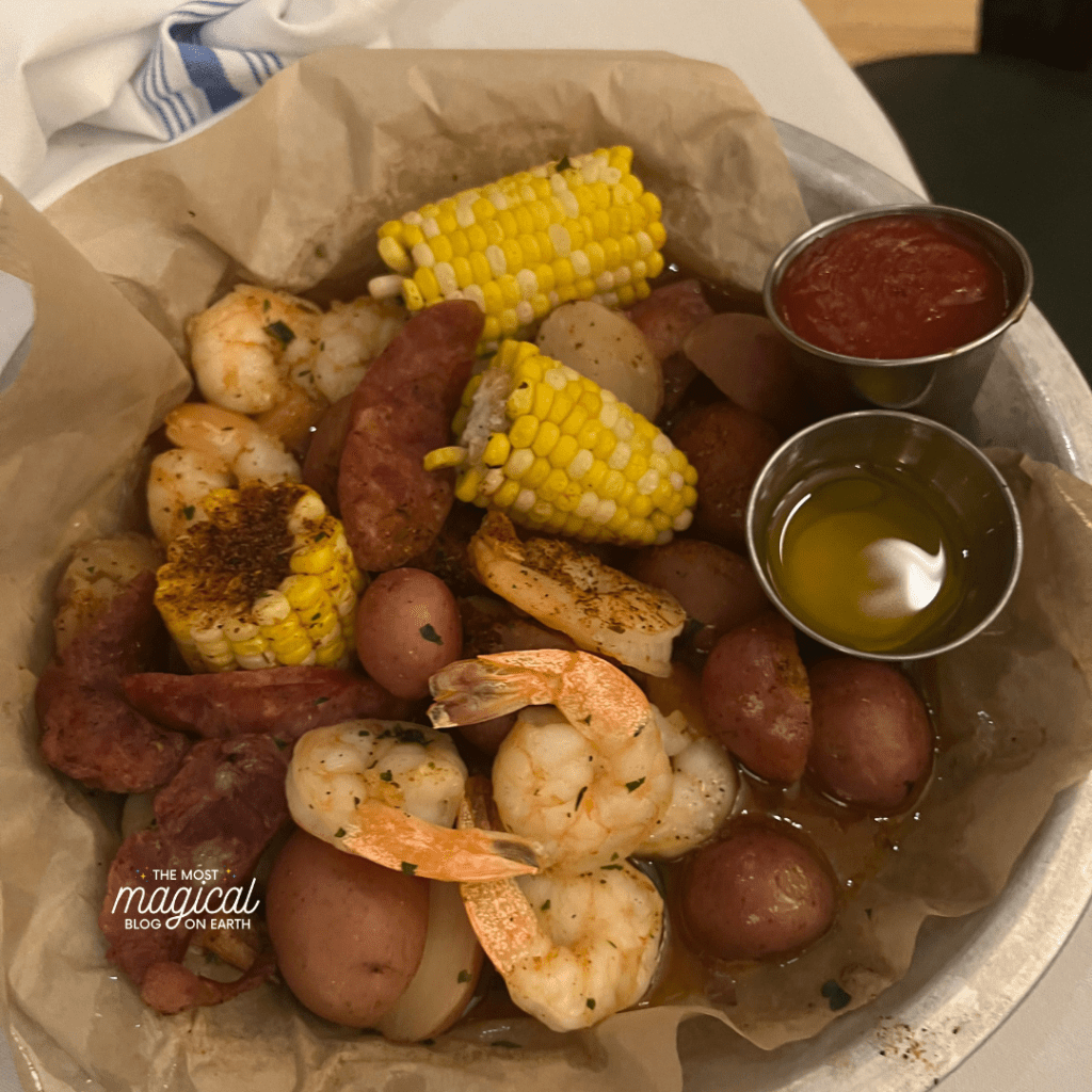 shrimp, sausage, potatoes, yellow corn, cups of butter, cups of cocktail sauce, in a bowl with paper